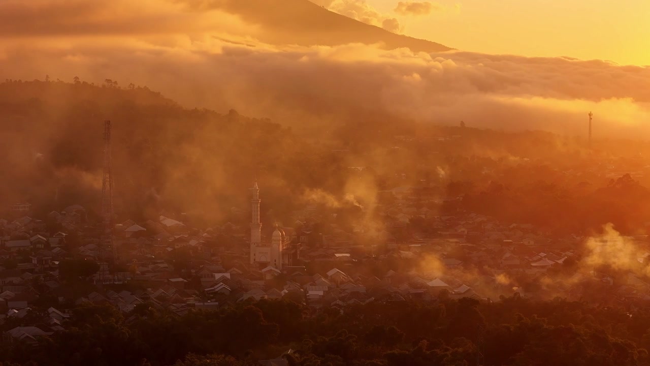Golden sunrise mist glows above Sembalun village beneath mountain clouds, aerial overview with mosque Masjid Ittihadul Islam Lawang at center