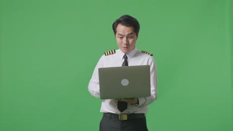 asian man pilot looking at a laptop then screaming goal celebrating while standing in the green screen background studio