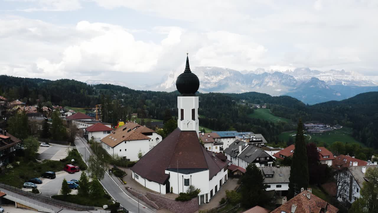 Rising aerial view of the local church overlooking Oberbozen, Italy's countryside