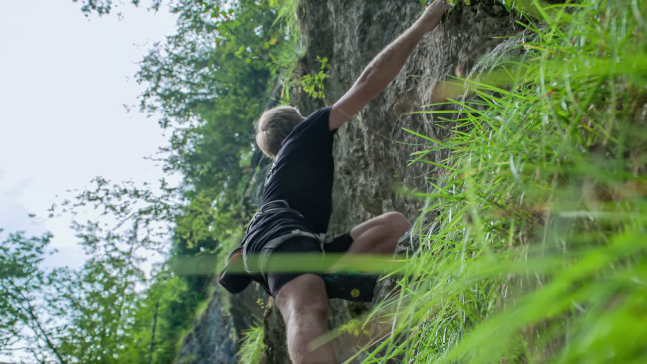 A low angle shot of a man climbing a steep mountain wall with no rope or safety equipment, just strength of his bare hands