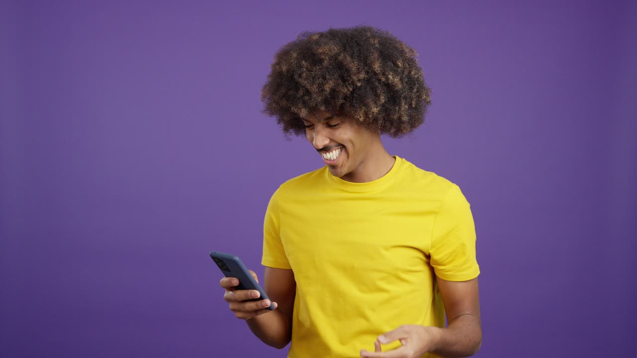 Happy man with afro hair checking phone while holding shopping bags