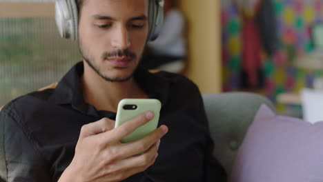 young hispanic man using laptop computer browsing online messages sharing network communication student enjoying listening to music checking smartphone social media in modern office