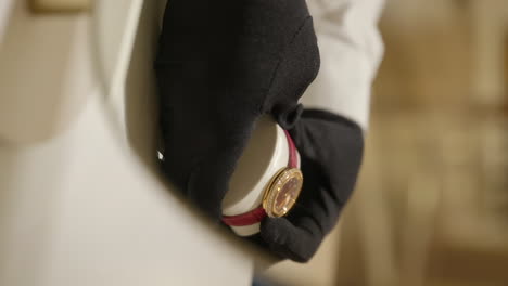 vertical shot of hands of salesperson rotating bezel of an expensive piaget women's watch embellished with diamonds and gold metal at the shop