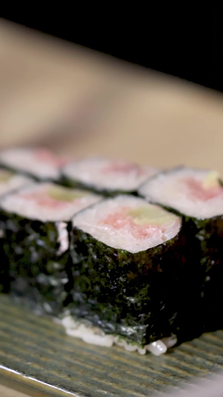 Nærbillede af hænder, der placerer friske maki sushi-ruller på en tekstureret grøn keramisk tallerken.