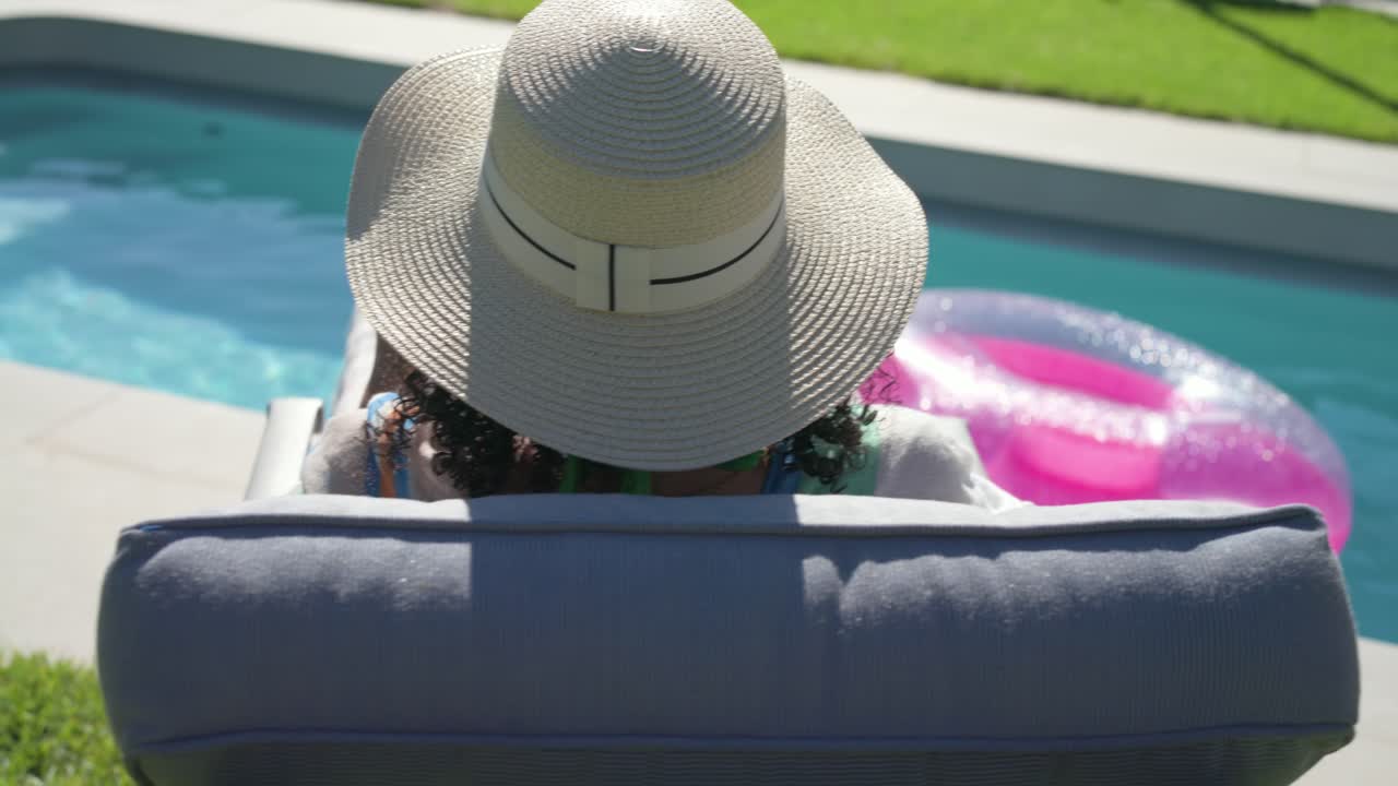 Woman is reclining on pool lounger, reading and turning pages as camera is pulling back, relaxing
