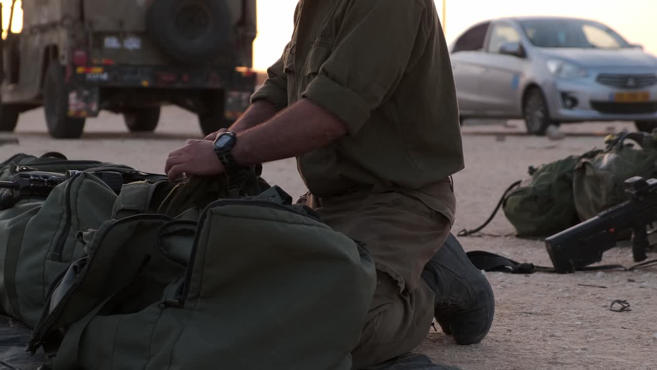 Close-up of soldiers hands prepare his equipment in his military bag ready to war while in the backround there are some vehicles