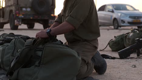 close-up of soldiers hands prepare his equipment in his military bag ready to war while in the backround there are some vehicles