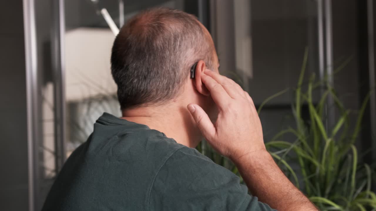 Adult man putting his hearing aids in his ears at home