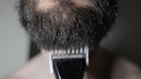 man trimming thick beard with electric groomer in slow motion