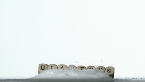 white dice spelling out diabetes falling over pile of sugar on white background