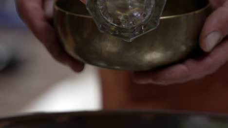 una mano con un vidrio transparente recoge agua de un plato de chladni y la agrega a un cuenco de canto para un baño de sonido en el valle sagrado, región de cuzco, perú - de cerca