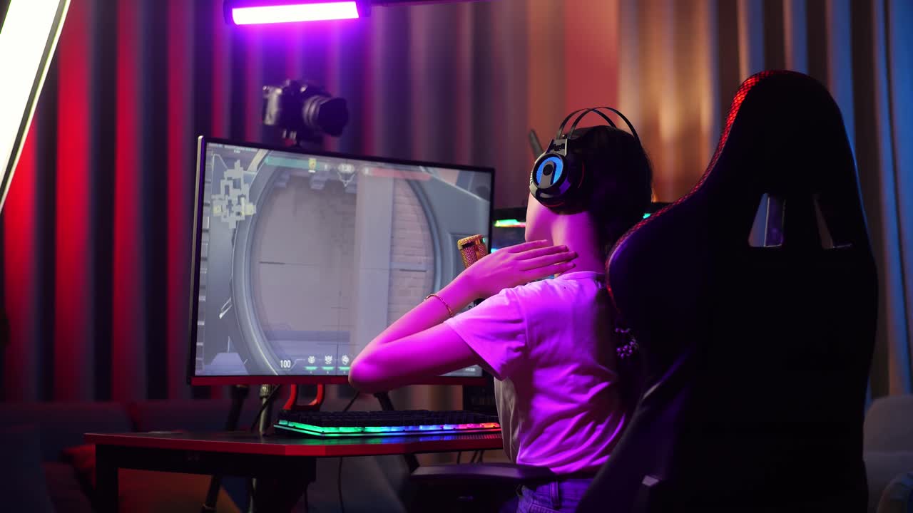 Back View Of Asian Girl Streamer Having A Backache While Playing Game Over Network On Personal Computer. Live Stream Video Game, Desk Illuminated By Rgb Led Strip Light