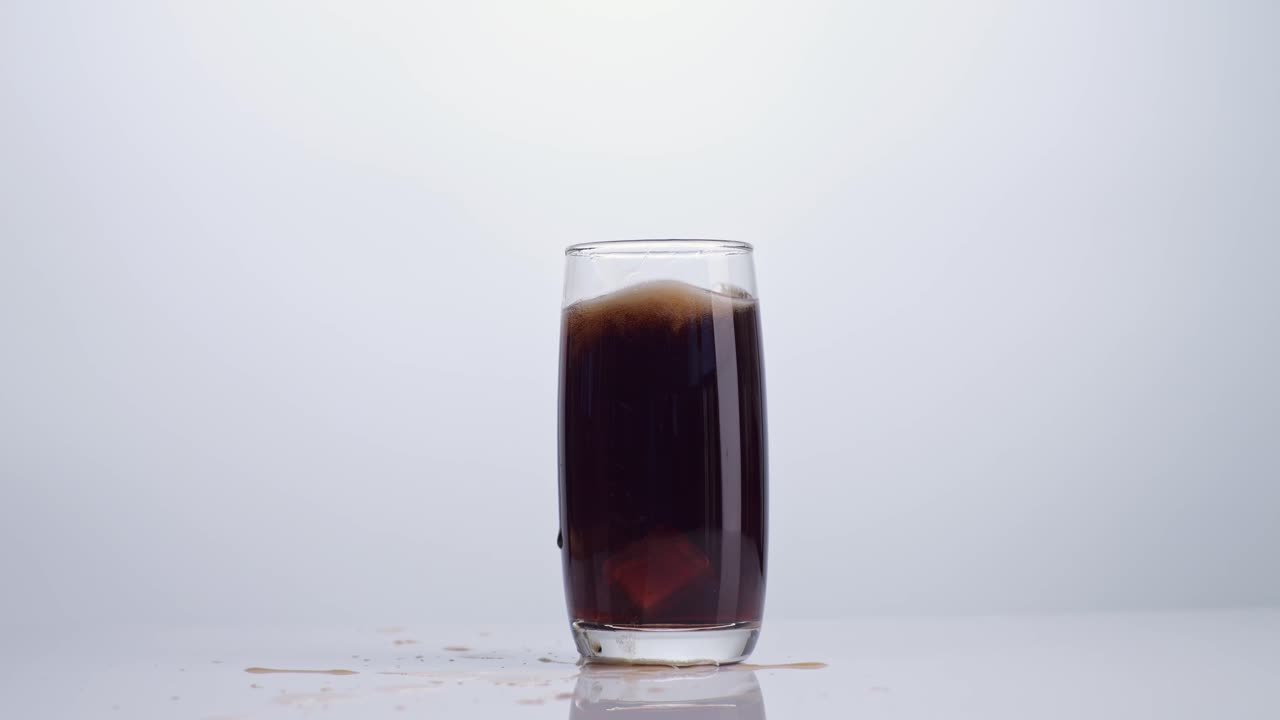 cubos de hielo cayendo en un vaso de cola fresca sobre un fondo blanco