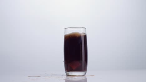 ice cubes falling in a glass of fresh cola on white background