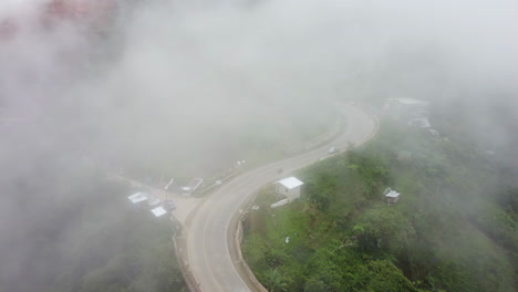 Revealing-aerial-footage-of-a-road-in-the-fogg-tilting-up-revealing-a-mountain-with-tropical-rainforest-in-the-Philippines,-Asia,-Drone