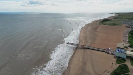 Typischer-Englischer-Badeort,-Aufgenommen-Mit-Einer-Drohne,-Die-Einen-Hohen-Luftbildpunkt-Bietet,-Der-Einen-Weiten-Sandstrand-Mit-Einem-Pier-Und-Tosenden-Wellen-Zeigt