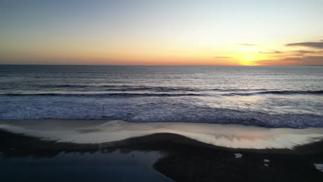 A-beautiful-sunset-in-the-South-of-Bali-looking-across-the-vast-seascape-with-a-coconut-tree-in-the-foreground,-aerial