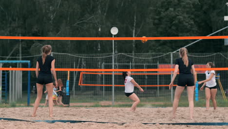 four girls volleyball players play on the beach in the summer participating in the tournament in slow motion on the sand