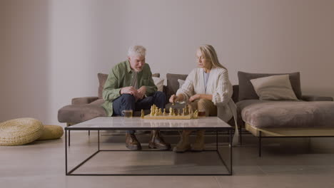 senior man and woman playing chess while sitting on sofa at home 1