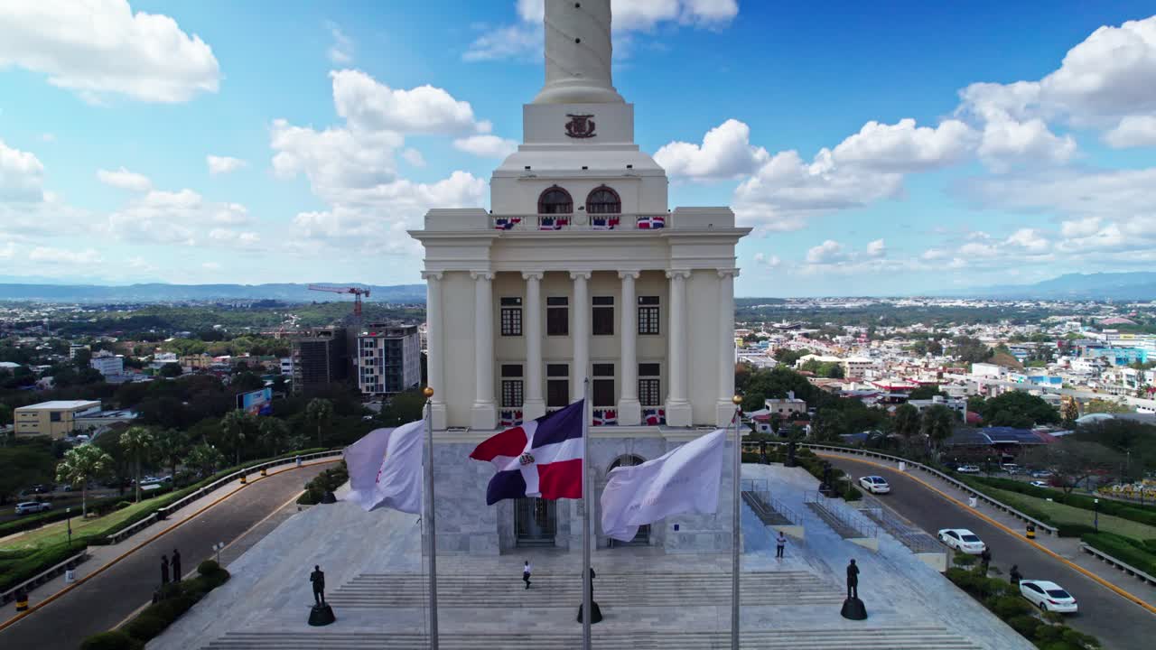 Plano pedestal de drone revelando o Monumento aos Heróis da Restauração. Movimento vertical da base arquitetônica e bandeiras tremulantes até o pináculo da torre sob um céu azul ensolarado