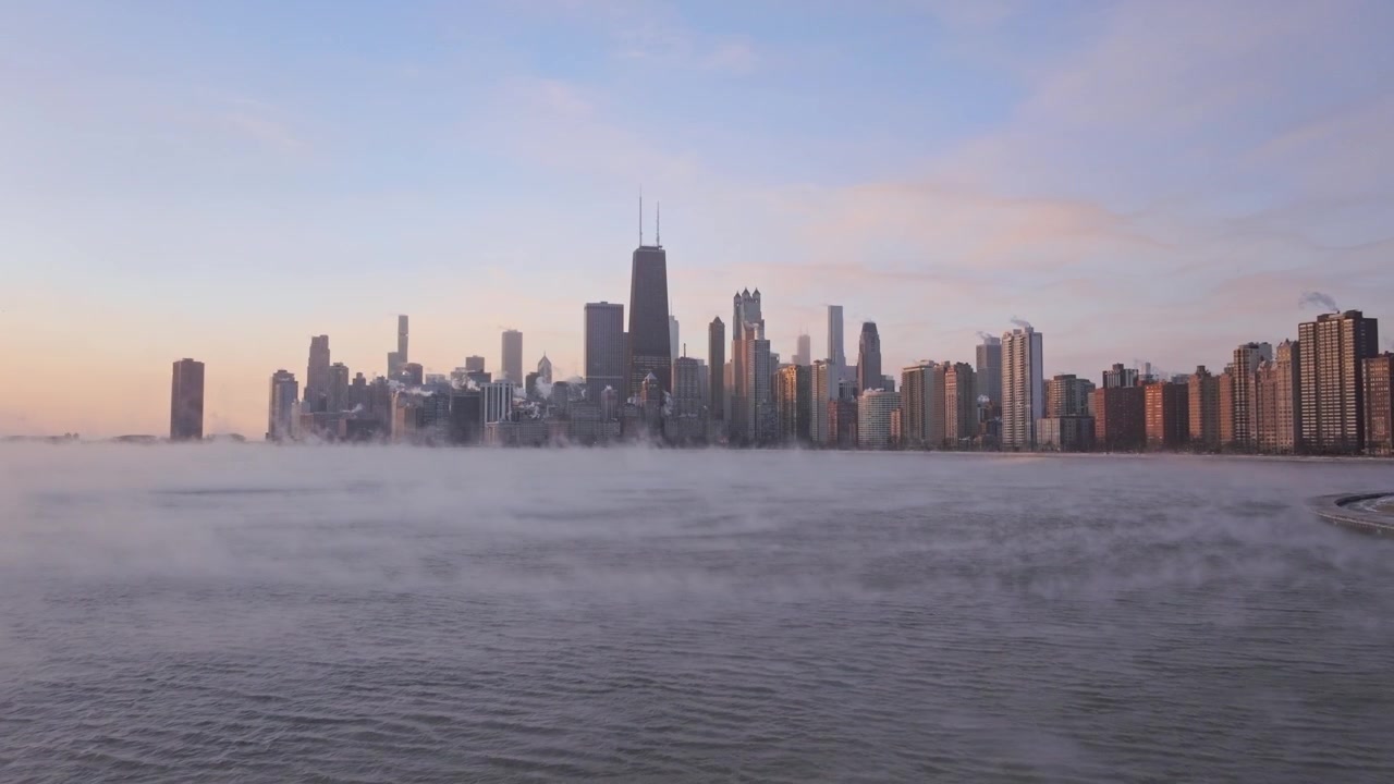 Tomada ampla de drone do horizonte de Chicago ao nascer do sol durante um severo vórtice polar de inverno, capturando fumaça marítima densa e névoa de vapor rolando sobre as águas congelantes do Lago Michigan