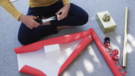 midsection of biracial woman sitting on floor packing christmas presents, slow motion