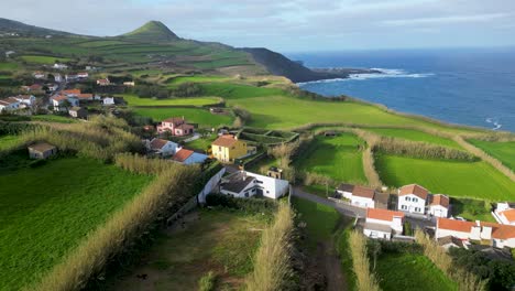 aerial panorama capturing quaint houses nestled amidst vibrant green fields in the azores on a sunny day, overlooking the azure expanse of the atlantic ocean