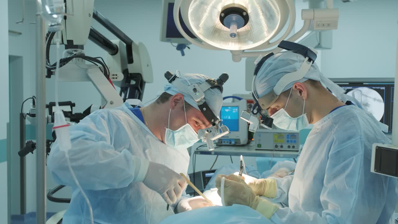 외과 의사는 수술을 수행하고 이동 현미경을 통해 볼 수 있습니다.
