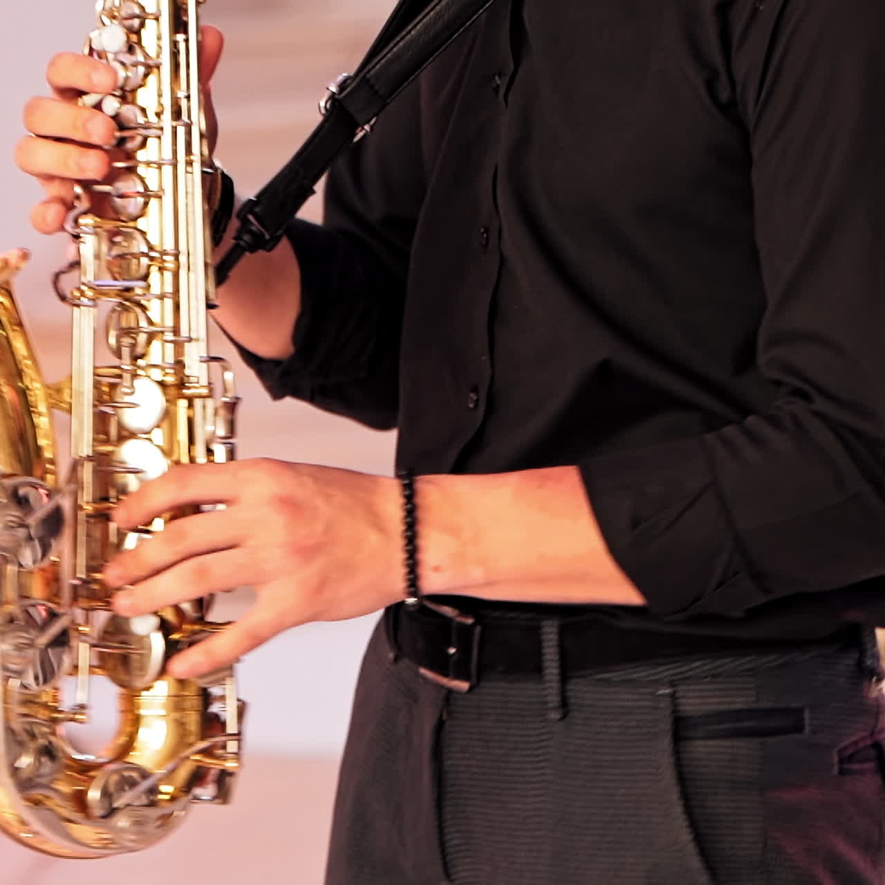 Saxophonist plays on golden saxophone indoors. A young man in black clothes is playing on a modern sax with microphone at the party. Jazz music. Close-up