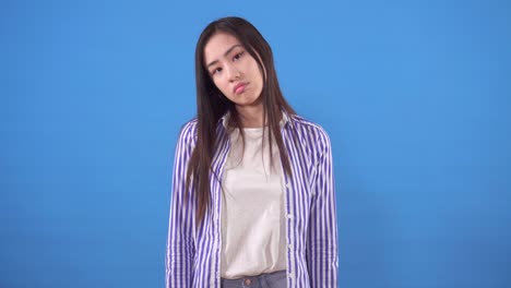 푸른 배경에 그녀의 머리의 부정적인 흔들림으로 셔츠를 입은 예쁜 젊은 아시아 여성