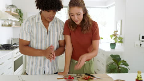 in kitchen, diverse couple eating homemade pancakes with strawberries, smiling together, at home