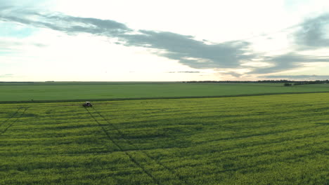 Tractor-spraying-fungicide-on-canola-in-field,-long-shot