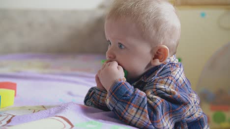 Lustiges-Baby-Im-Hemd-Knabbert-An-Einem-Grünen-Würfel,-Der-Sich-Auf-Ein-Weiches-Bett-Stützt