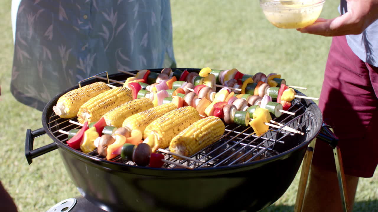 Grilling colorful vegetable skewers and corn on barbecue grill at in garden picnic