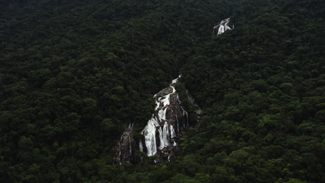 Drone-shot-overlooking-a-waterfall,-in-the-jungles-of-cloudy-Barro-da-Sahy,-Brazil