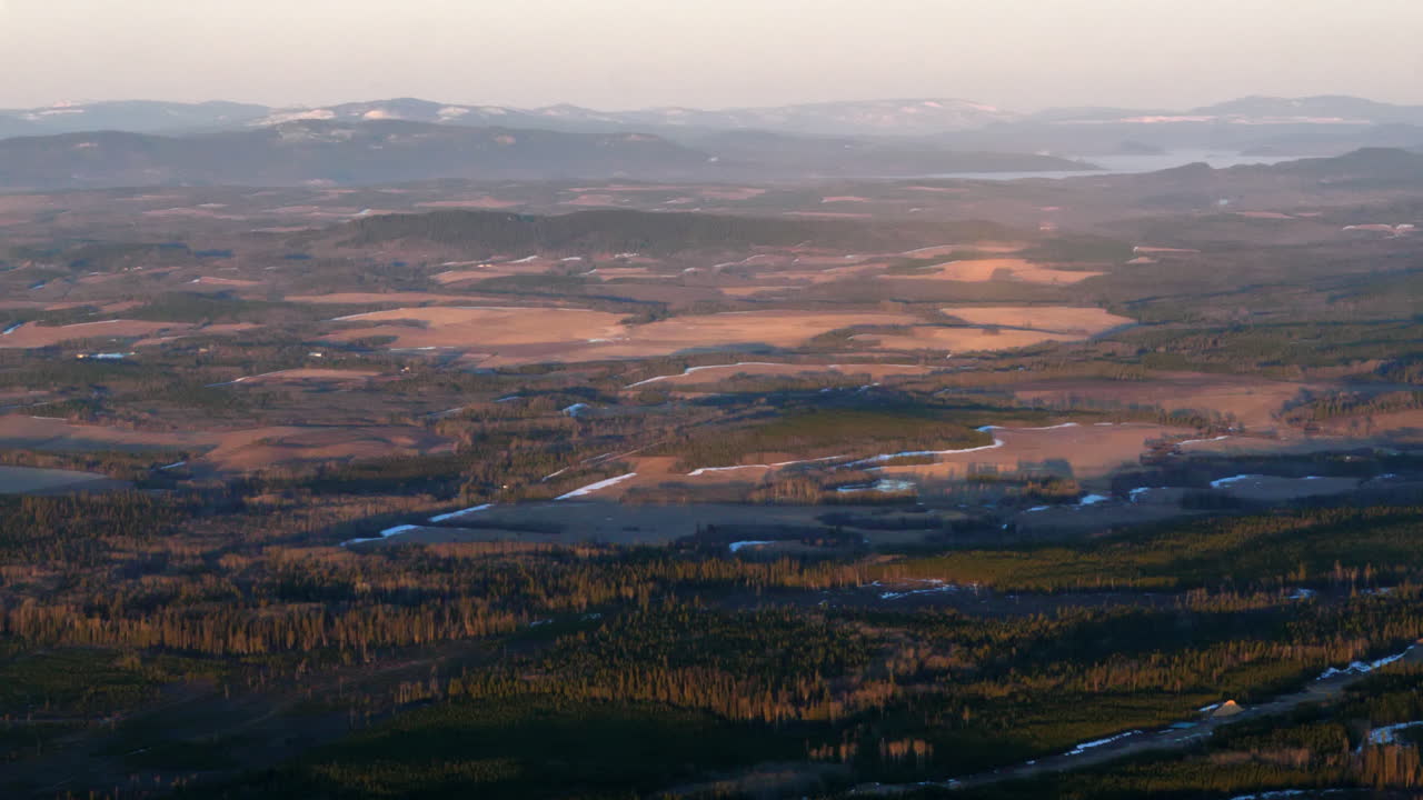 Panorama af landligt terræn med skovpark og bjergkæder i baggrunden under en tåget morgen