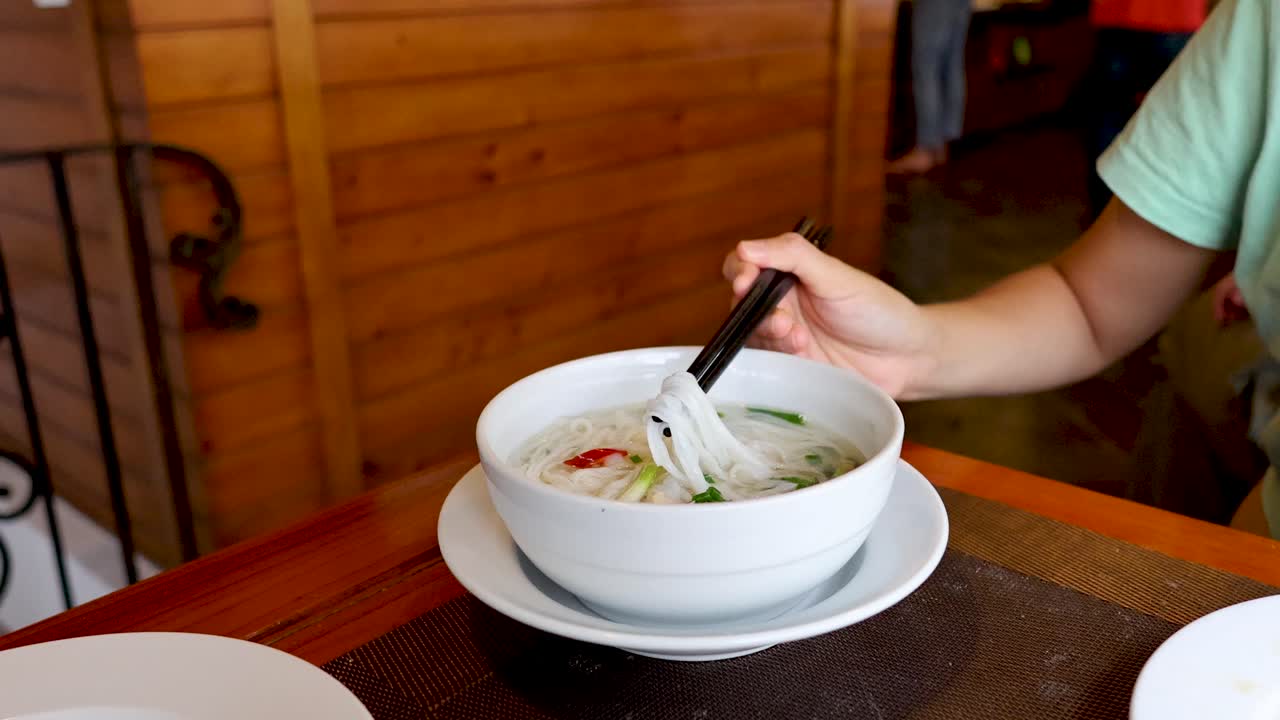한 사람이 테이블에서 스틱으로 누들 수프를 먹고 있다