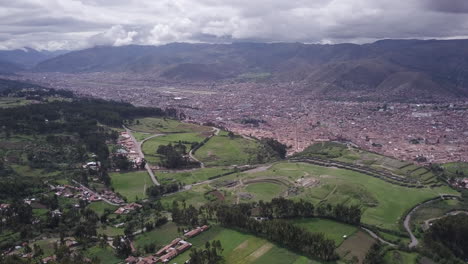 expansive aerial view of a city nestled in a valley surrounded by green fields and mountains under a cloudy sky