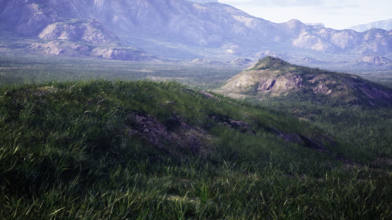 Rolling hills with lush grass and distant mountains under clear skies
