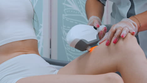 young woman in white bathrobe on laser hair removal procedure in beautician clinic slow motion. doctor removes hair from legs or body of patient. concept