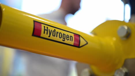 The-word-hydrogen-is-written-on-a-yellow-pipe-which-is-part-of-a-demonstrator-of-special-shut-off-valves-on-a-trade-fair,-people-talking-in-the-background