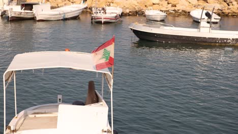 lebanon flag waving in the wind on small fishing boat in mediterranean harbor near tripoli, northern lebanon