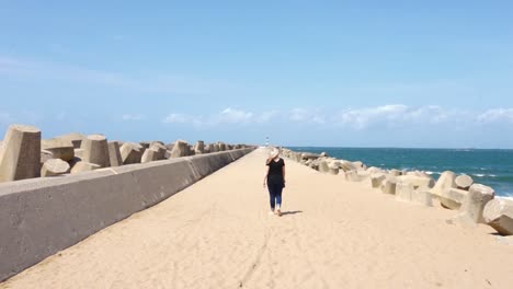 chica rubia caminando por un muelle con sus zapatos en la mano de espaldas a la cámara