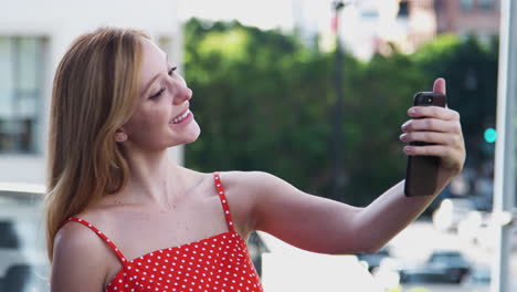 young businesswoman having video chat on mobile phone standing outside city office building