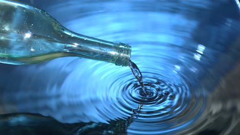 botella de vidrio vertiendo agua en agua azul