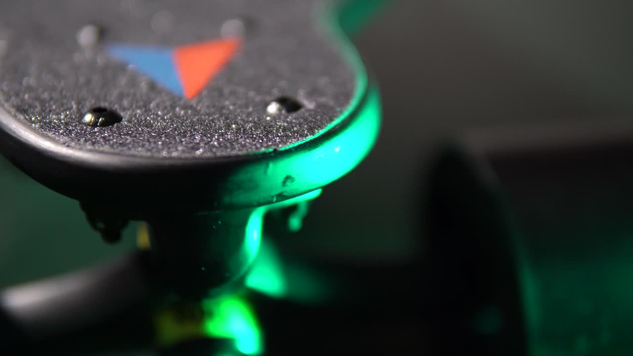 detail of a tip of an electric longboard lit by a creative green light, dolly in, rack focus