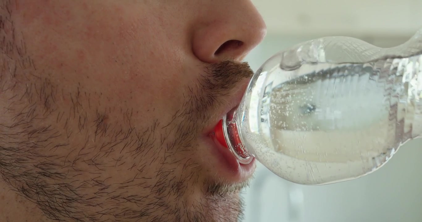 Homem bebendo água diretamente de uma garrafa de plástico com a abertura da garrafa completamente dentro da boca. Adequado para conceitos de hidratação, sede, hábitos de consumo, refresco, estilo de vida e bebidas.