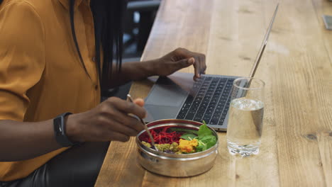 Joven-Empresaria-Trabajando-En-Una-Computadora-Portátil-Mientras-Almuerza-En-El-área-De-Cantina-De-Una-Oficina-Moderna