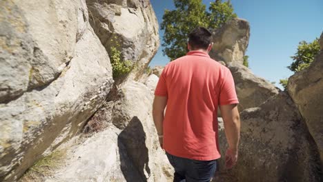 Tourist-walking-up-the-rocky-trail-of-the-ancient-city-of-Perperikon,-while-holding-on-the-rock-wall-of-this-historical-landmark-located-in-the-province-of-Kardzhali-in-Bulgaria