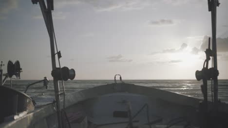 a view on the sea and the sunset from a fishing boat parked on the shore - trucking shot from left to right during the golden hour - ending with the sun hiding behind a panel